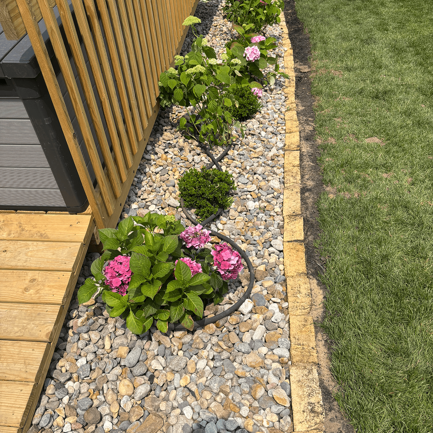 Flower bed with rock ground cover, decorative edging, and shrubs installed near a deck in Central Iowa.