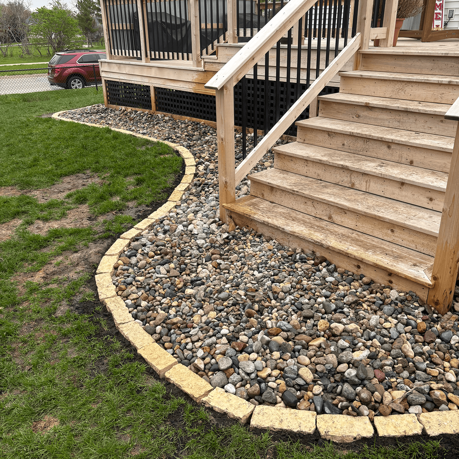 River rock landscaping with curved stone edging along a backyard deck near Ankeny.