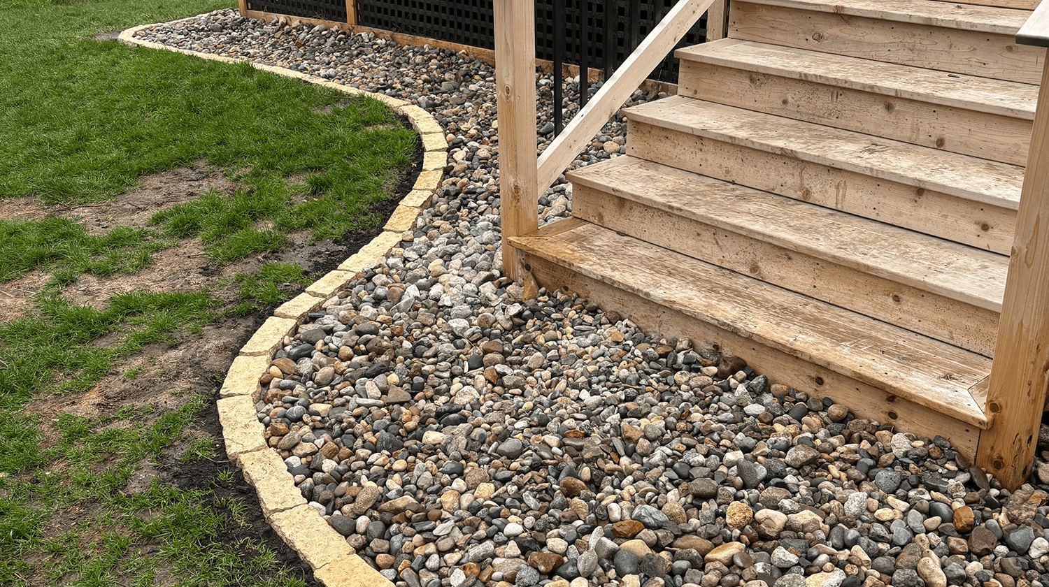 New landscape installation featuring decorative river rock and concrete edging along backyard stairs.