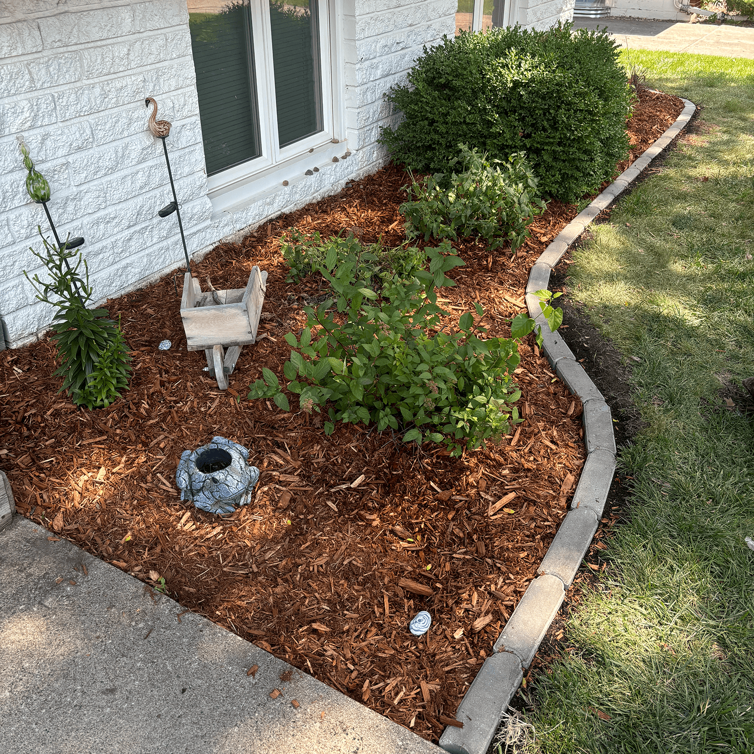 Fresh mulch bed installation along a home foundation with small shrubs and garden accents.