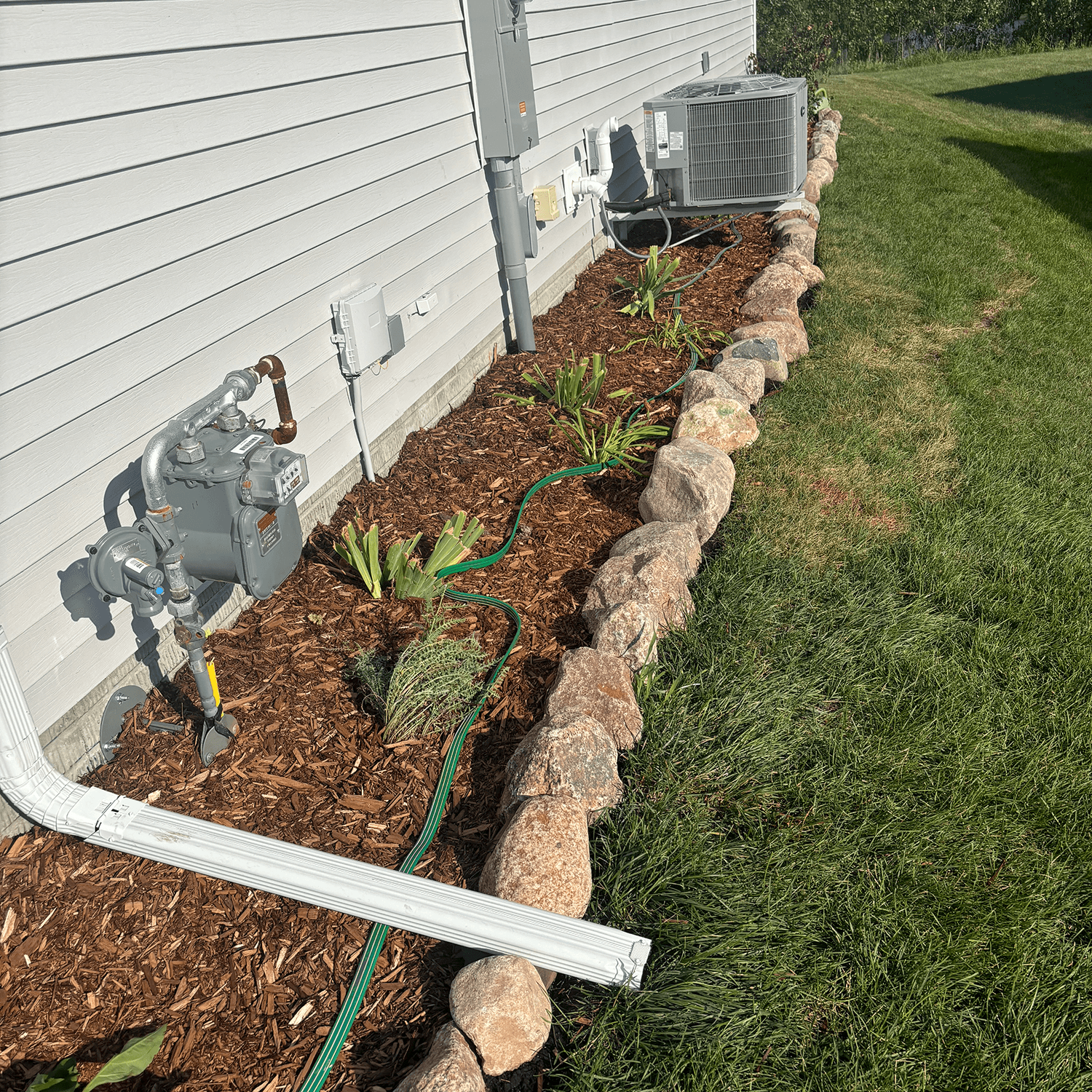 Mulch bed and plant installation along a side yard with natural boulder edging in Ankeny, Iowa.